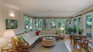 Ein Wintergarten mit großem Fenster, einer Couch, einem runden Couchtisch und einem Esstisch mit Stühlen.