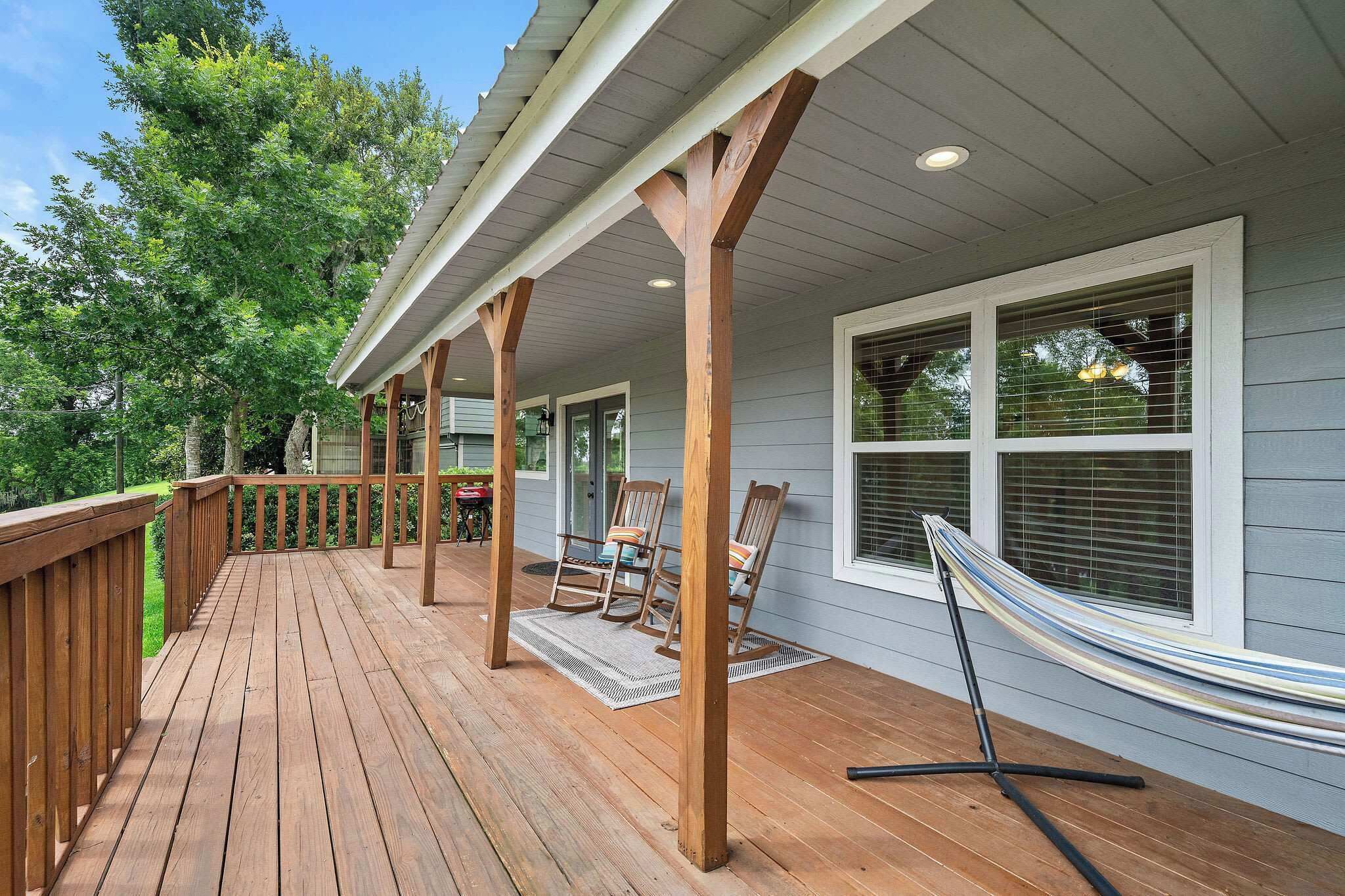 A wooden deck with a hammock, rocking chairs, and a covered porch area.