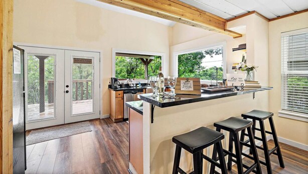 A kitchen with a wooden ceiling, a bar area with stools, and a view of the outdoors through large windows. - Riverfront Retreat w/ Decks & Views (Baytown)