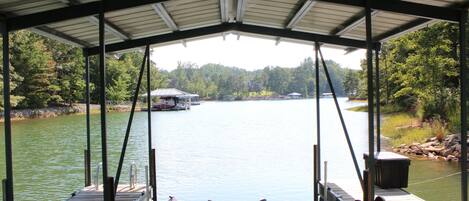 A covered dock with a view of a lake, boats, and forested area.