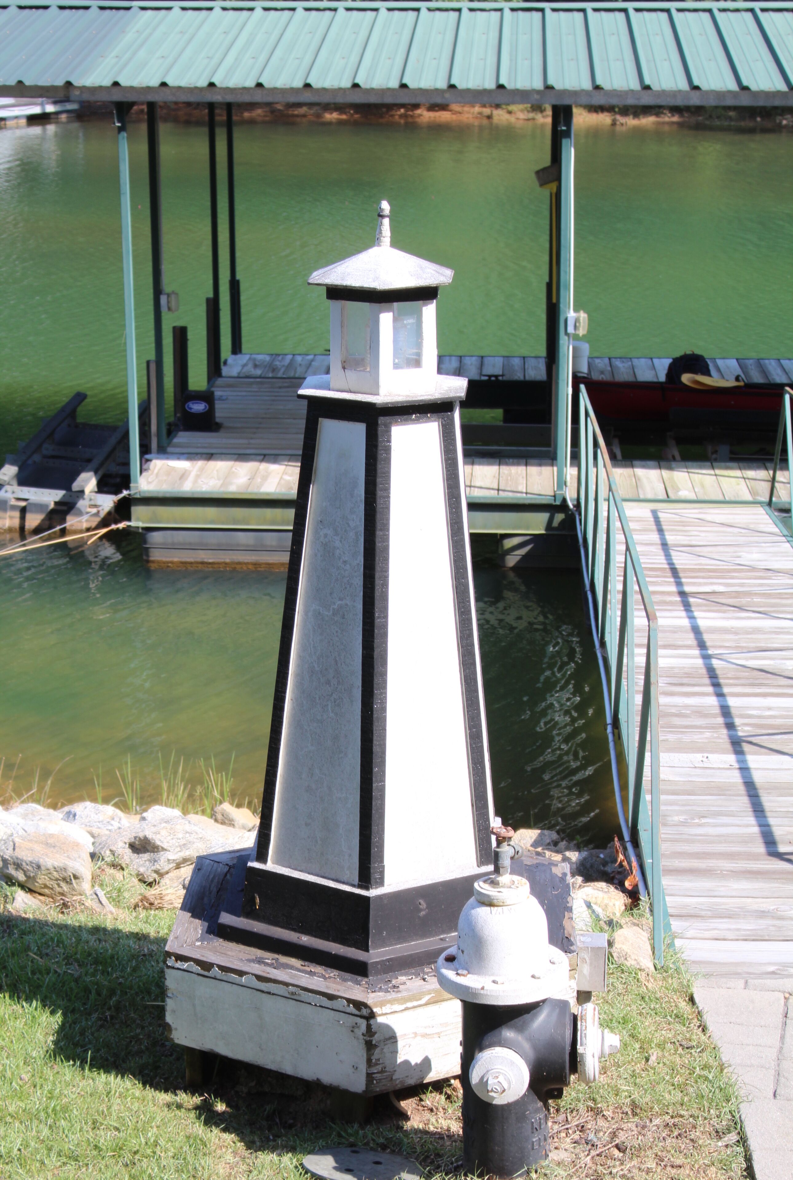 Une structure ressemblant à un phare, avec un motif noir et blanc, située sur un quai, au bord d’une étendue d’eau.
