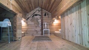 A log cabin interior with a central fireplace, wooden walls, a small white chair, and a table. - Log cabin for 4 + 2 people, 80m2 in the middle of the forest between 2 lakes (Hallaryd)