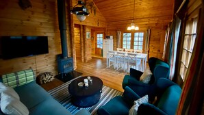 A cozy log cabin interior with a sofa, a coffee table, a fireplace, a dining area, and a television. - Log cabin for 4 + 2 people, 80m2 in the middle of the forest between 2 lakes (Hallaryd)