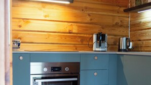 A compact kitchen with wooden walls, a built-in oven, and a coffee maker on the countertop. - Log cabin for 4 + 2 people, 80m2 in the middle of the forest between 2 lakes (Hallaryd)