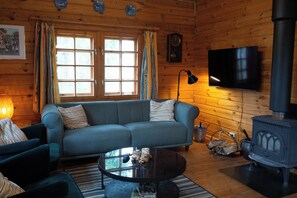 A cozy log cabin interior with a sofa, a television, a fireplace, and a window with curtains.