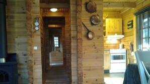 A wooden cabin interior with a central hallway leading to a kitchen area. - Log cabin for 4 + 2 people, 80m2 in the middle of the forest between 2 lakes (Hallaryd)