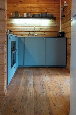 A compact kitchen with wooden flooring, a built-in oven, and a sink. - Log cabin for 4 + 2 people, 80m2 in the middle of the forest between 2 lakes (Hallaryd)