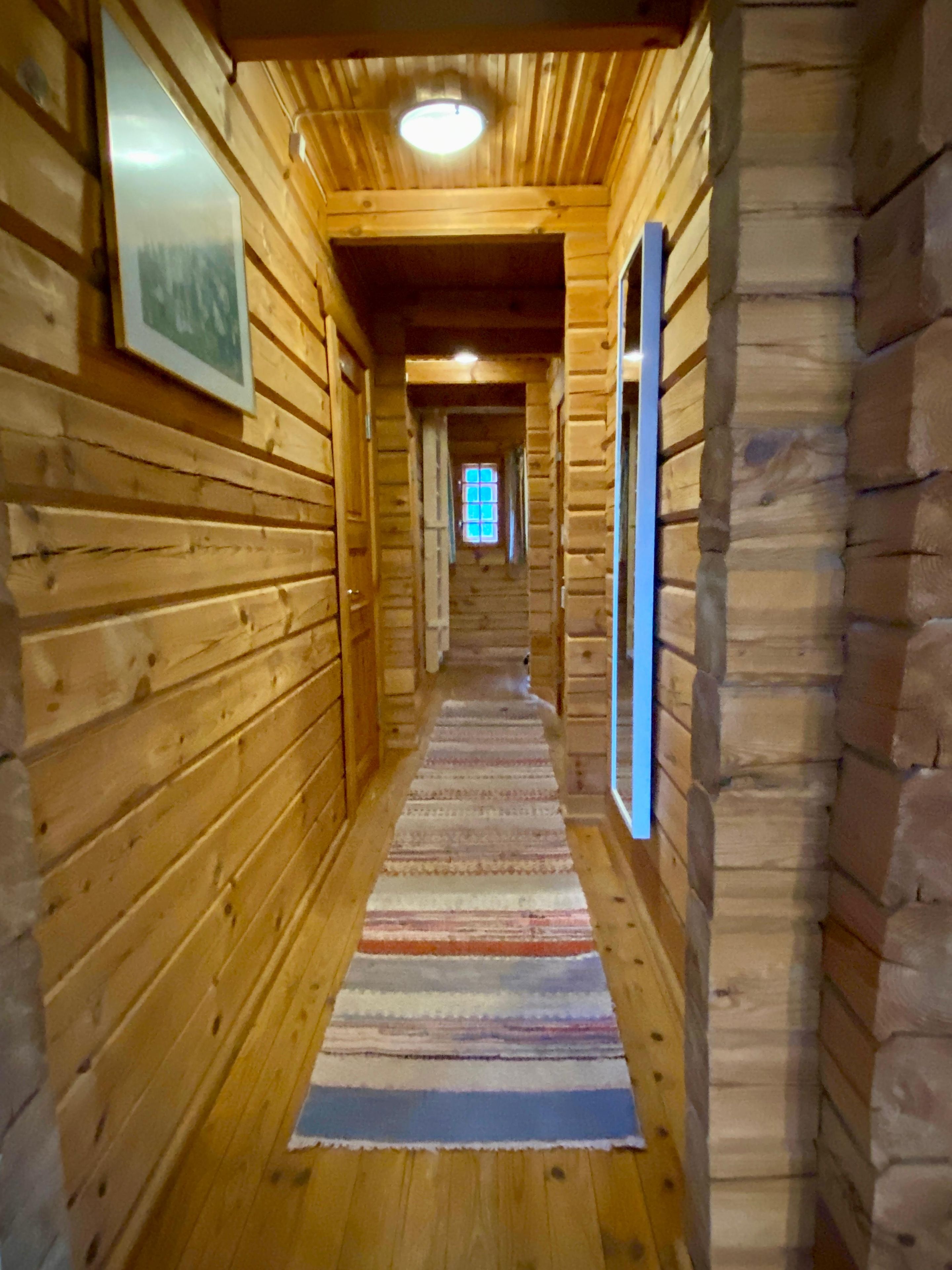Un pasillo de madera con un tapete a rayas, paredes de madera y una ventana al final.