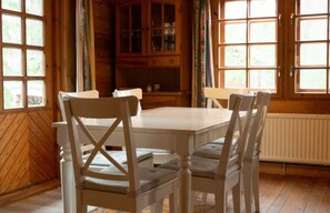 Un espace repas avec une table et des chaises blanches, des meubles en bois et de grandes fenêtres.