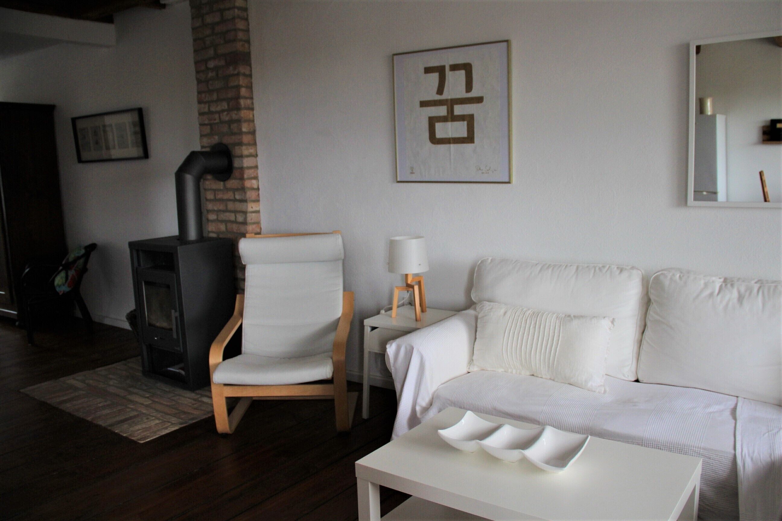 A living room with a white sofa, a white armchair, a white coffee table, a fireplace, and a framed artwork on the wall.