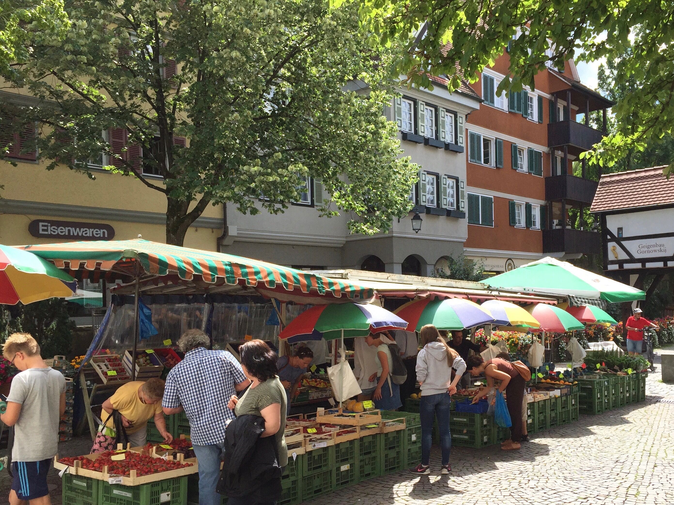Een levendige buitenmarkt met verkopers die fruit en groenten aanbieden onder kleurrijke parasols.