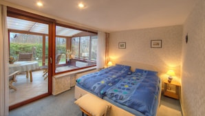 A bedroom with a large bed, a window with a view of the garden, a table with chairs, and a lamp on the bedside table. - Family-friendly holiday paradise 120m² modern equipment, close to the beach (500m) (timmendorfer strand)