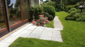 A modern house with a large glass window, a stone pathway, and a well-maintained garden with pink flowers and green grass. - Family-friendly holiday paradise 120m² modern equipment, close to the beach (500m) (timmendorfer strand)
