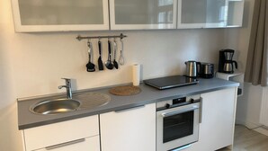 A compact kitchen with a stainless steel sink, a kettle, a coffee maker, and a microwave. There are cabinets with frosted glass doors and a set of hanging utensils. - 2-room apartment II "Am Nonnenhaus", old town near the university for up to 4 people (Tübingen)
