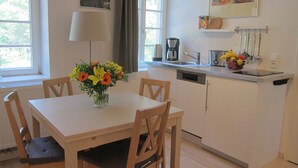A dining area with a table and chairs, a vase of flowers, a coffee maker, and kitchen utensils on the counter. - 2-room apartment II "Am Nonnenhaus", old town near the university for up to 4 people (Tübingen)