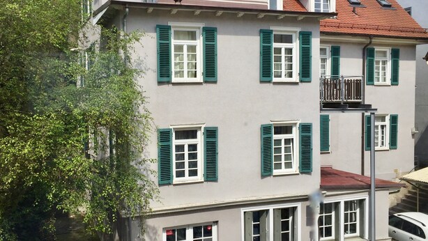 A multi-story building with green shutters, a red-tiled roof, and a visible balcony. - 2-room apartment II "Am Nonnenhaus", old town near the university for up to 4 people (Tübingen)
