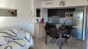 Een moderne keuken met donkere kastjes, een roestvrijstalen koelkast en een eethoek met een tafel en stoelen.