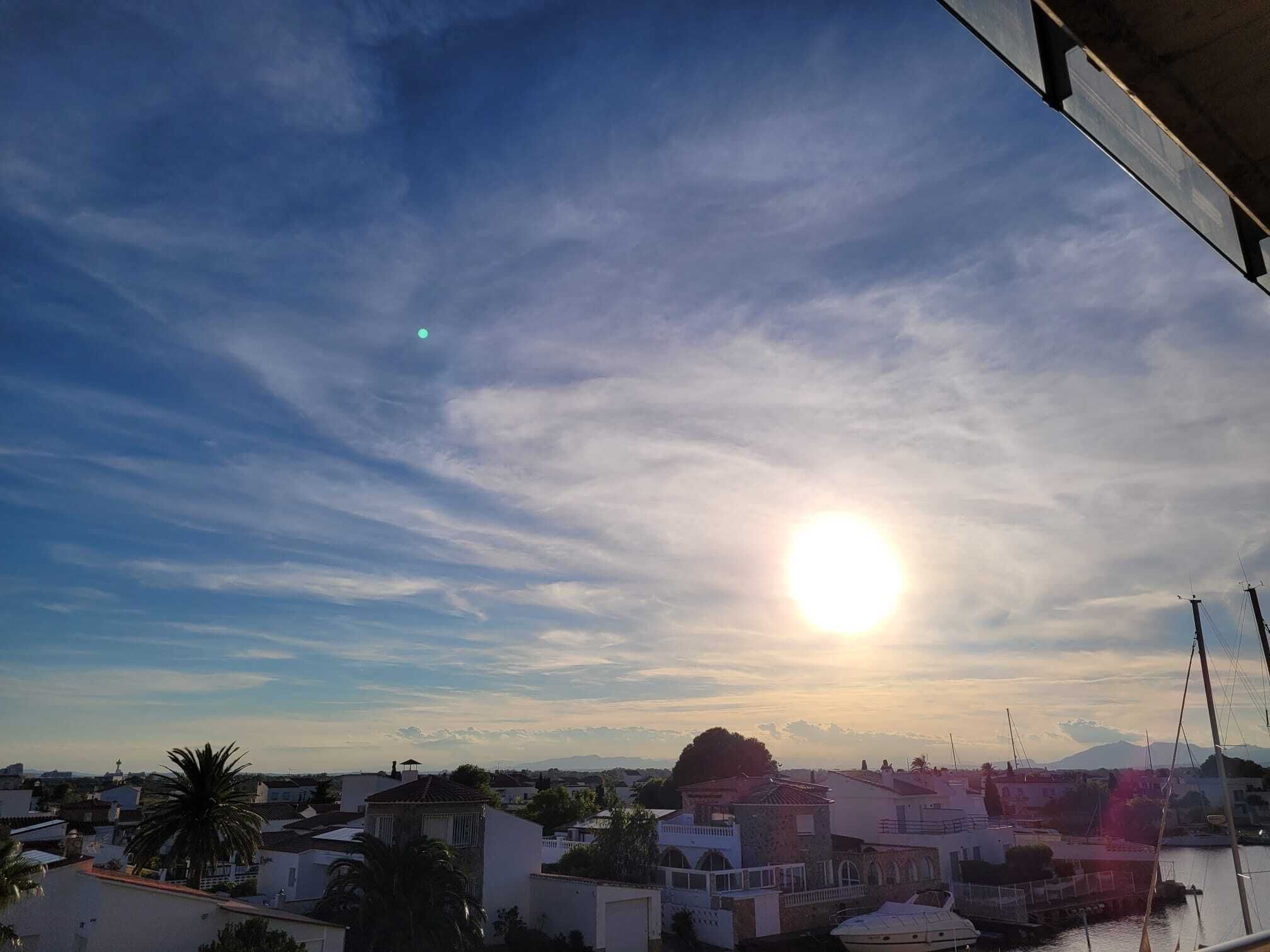 Un pueblo costero con edificios, cielo despejado y el sol poniéndose o saliendo.