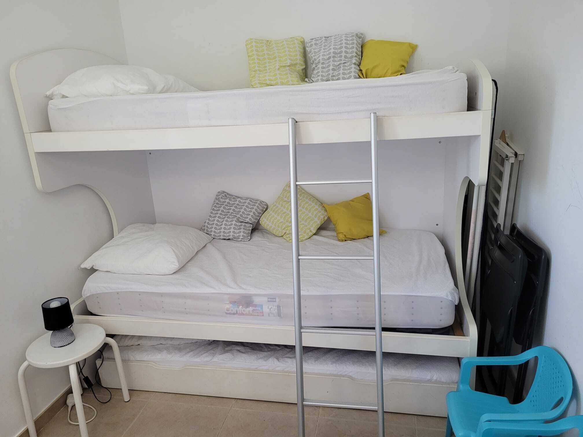 Een stapelbed met twee niveaus, een tafeltje met een lamp en een blauwe stoel.