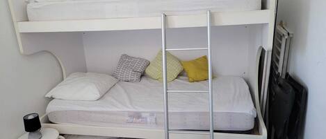 Een stapelbed met twee niveaus, een tafeltje met een lamp en een blauwe stoel.