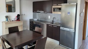 Een moderne keuken met donkere kasten, een roestvrijstalen koelkast, een magnetron, een koffiezetapparaat en een eettafel met stoelen.