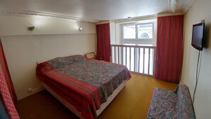 Un dormitorio con cama, una silla, televisor y ventana con cortinas.