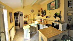 A kitchen with a tiled floor, a sink, a stove, and a microwave. There is a door leading to another room, and a clock on the wall. - Cosy air-conditioned vacation home by the sea, free bikes (Saint-Cyprien)