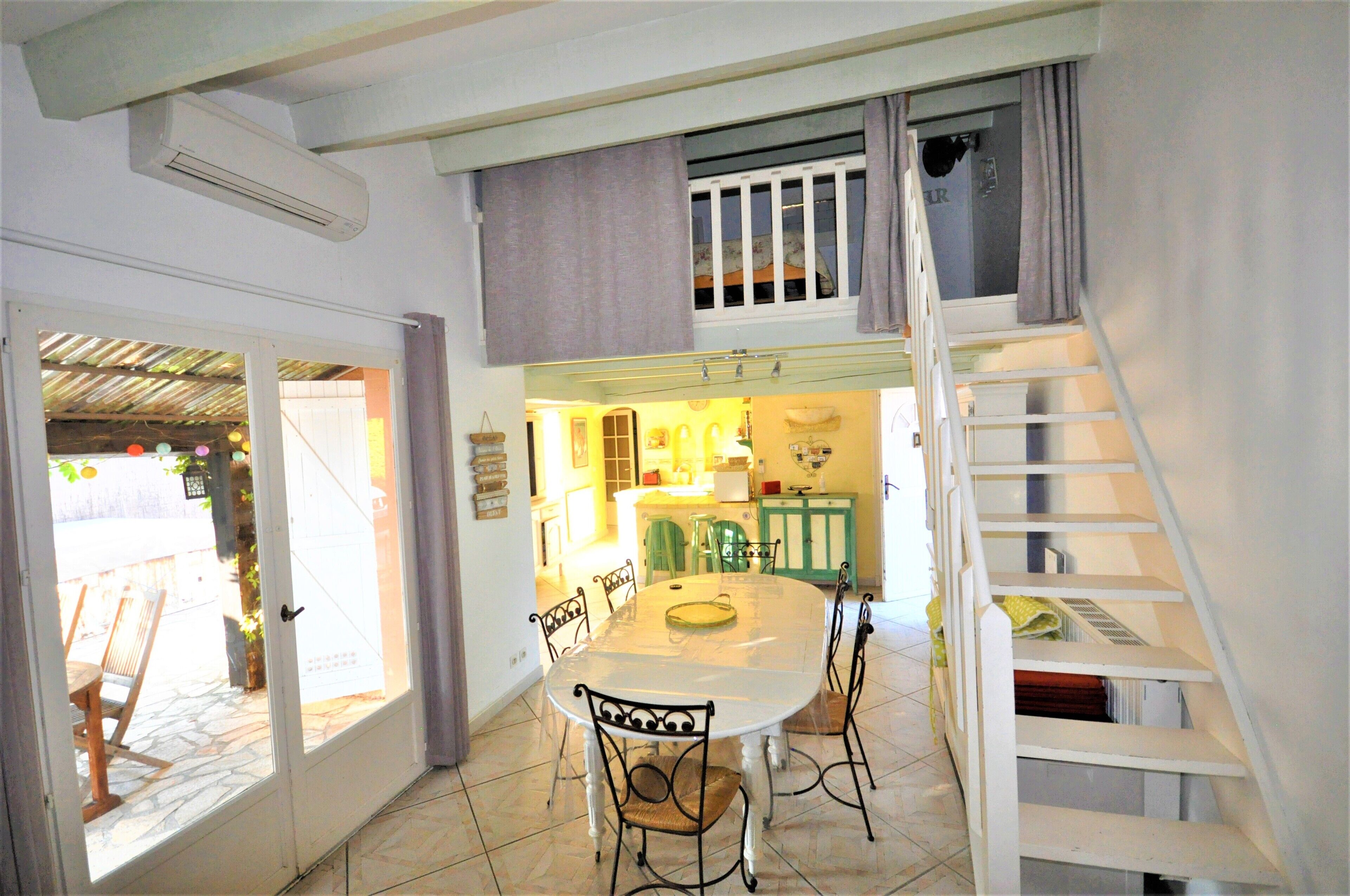 A dining area with a white table and chairs, a staircase, and a kitchen visible through an open door.