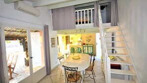 A dining area with a white table and chairs, a staircase, and a kitchen visible through an open door. - Cosy air-conditioned vacation home by the sea, free bikes (Saint-Cyprien)