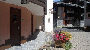 A hotel entrance with a stone-paved pathway, a wooden door, and a flower planter. - 3 * appt, 5 people in the heart of the resort, open to hikers out of season (Les Avanchers-Valmorel)