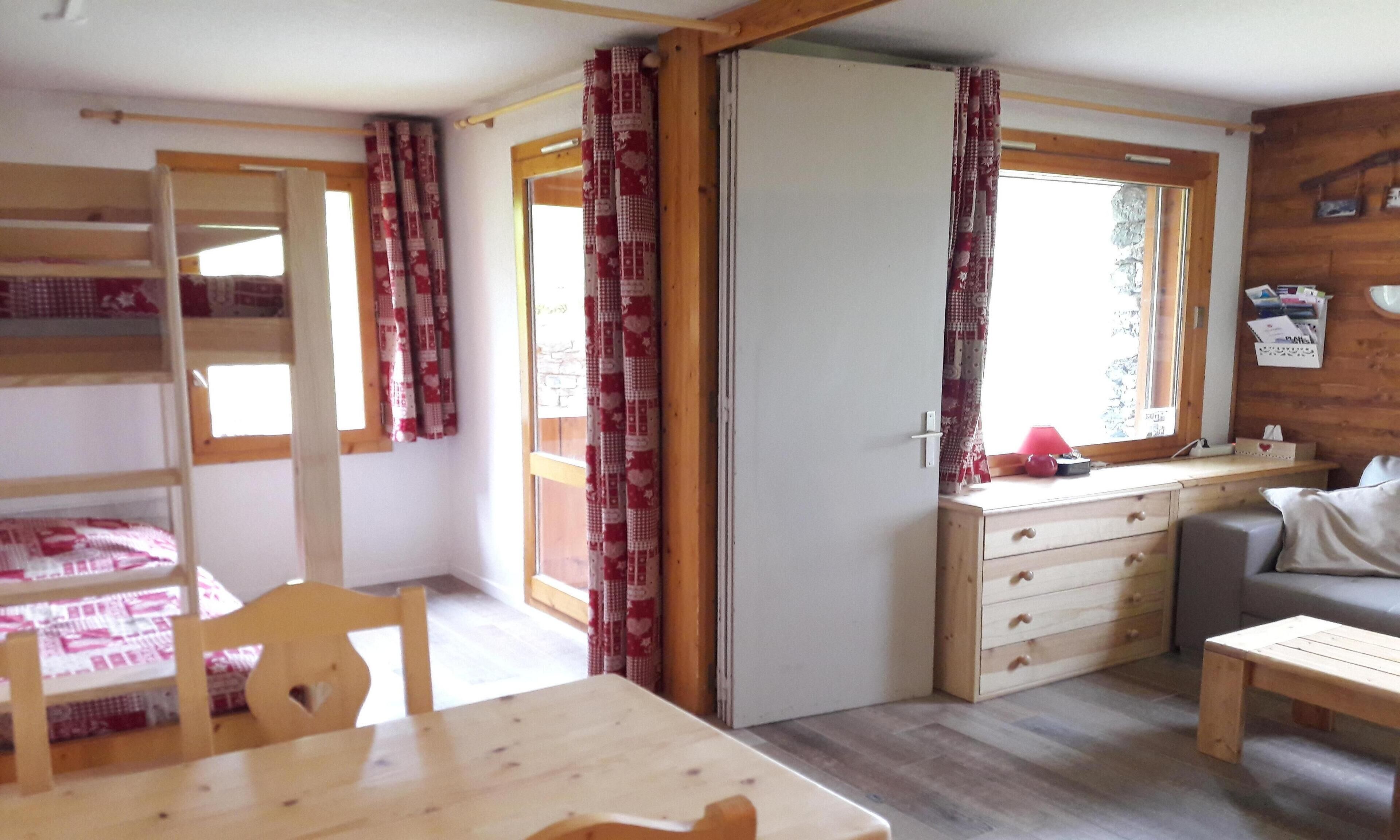 A cozy room with a wooden table, a sofa, a desk with drawers, and a bunk bed.