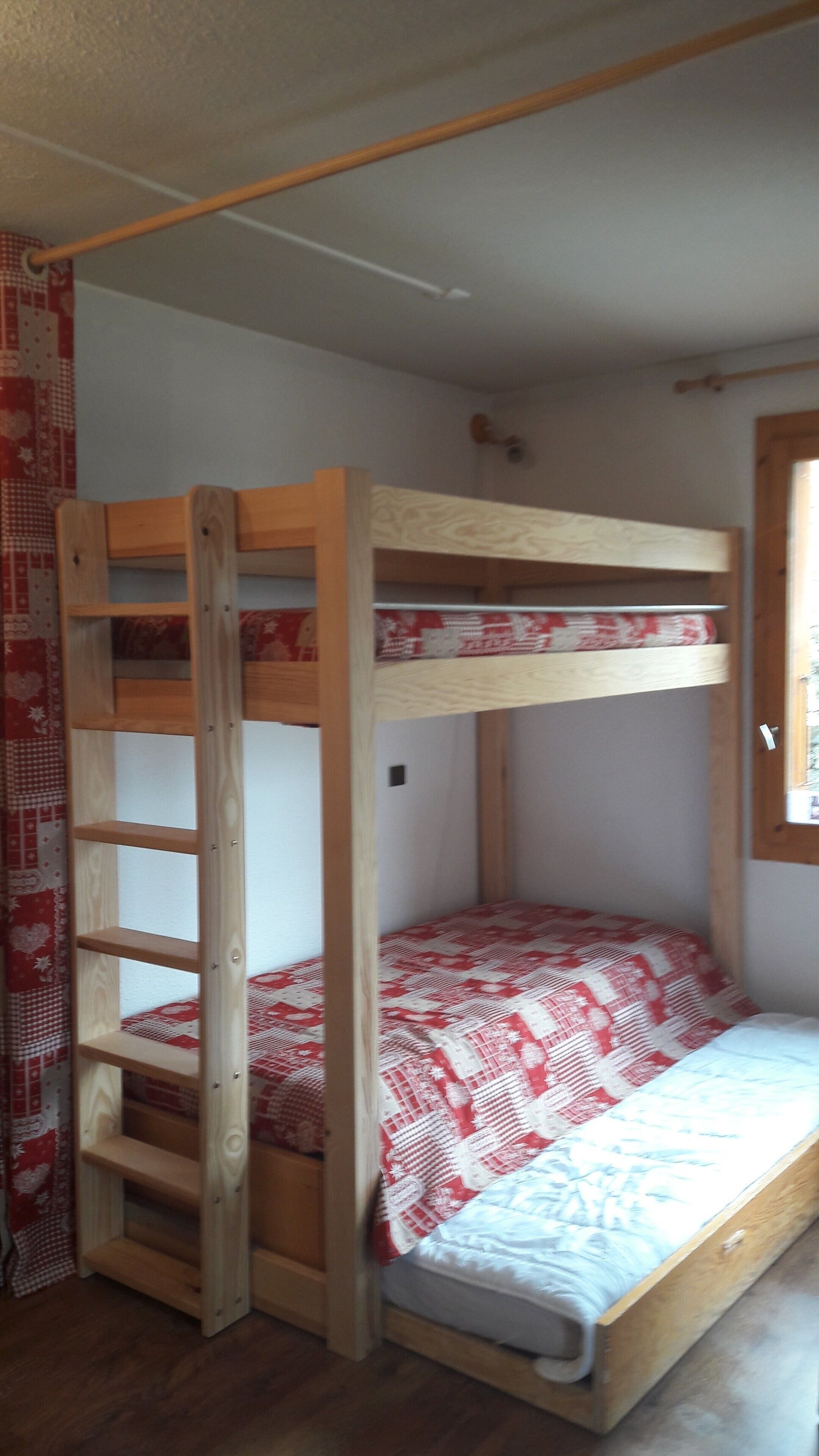 Ein Etagenbett mit einer Holzleiter und einer Bettdecke in Rot und Weiß.