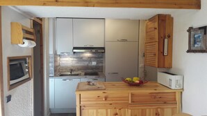 A compact kitchen with white cabinets, a built-in oven, and a microwave. There's a wooden countertop with a fruit bowl and a toaster. - 3 * appt, 5 people in the heart of the resort, open to hikers out of season (Les Avanchers-Valmorel)