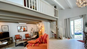 A spacious living room with a high ceiling, a balcony, and a staircase leading to an upper floor.
