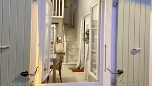 A narrow window with shutters, a staircase leading to an upper floor, and a view of a dining area with a table and chairs.