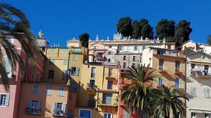 A multi-story building with balconies, a palm tree in the foreground, and a clear blue sky.