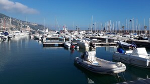 A marina with various boats docked, a lighthouse in the background, and calm water. - --- Beachfront Studio ---- (Menton)
