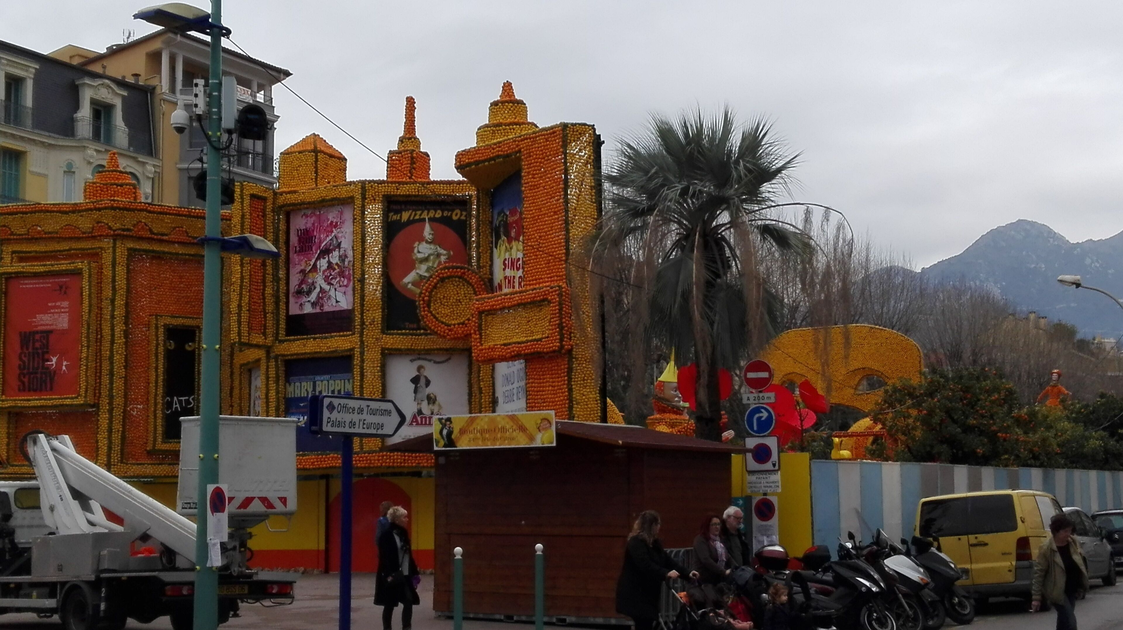 Um edifício com exterior único em tons de laranja e amarelo, exibindo diversos cartazes e placas, incluindo um para 'The Wizard of Oz'.