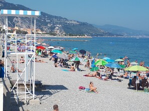 A crowded beach with umbrellas and people sunbathing.