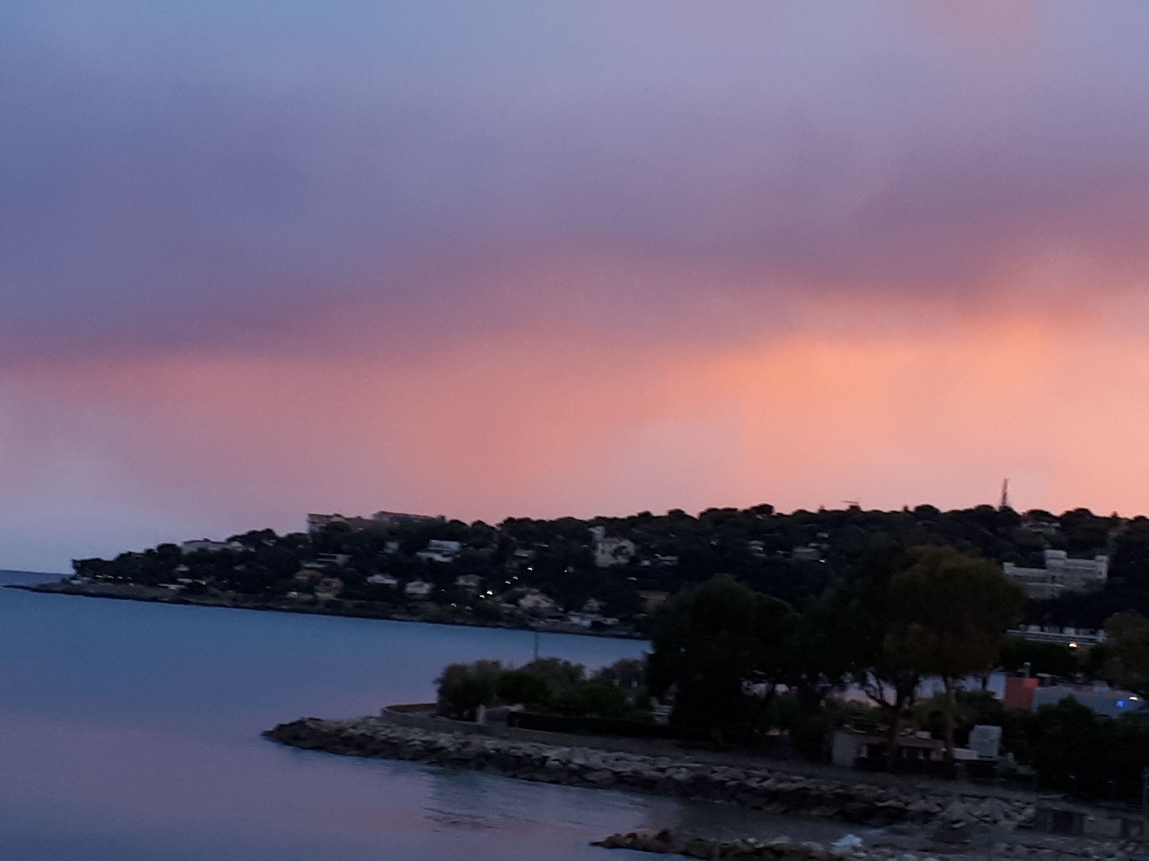 A coastal town with buildings along the waterfront, a rocky breakwater, and a calm sea.