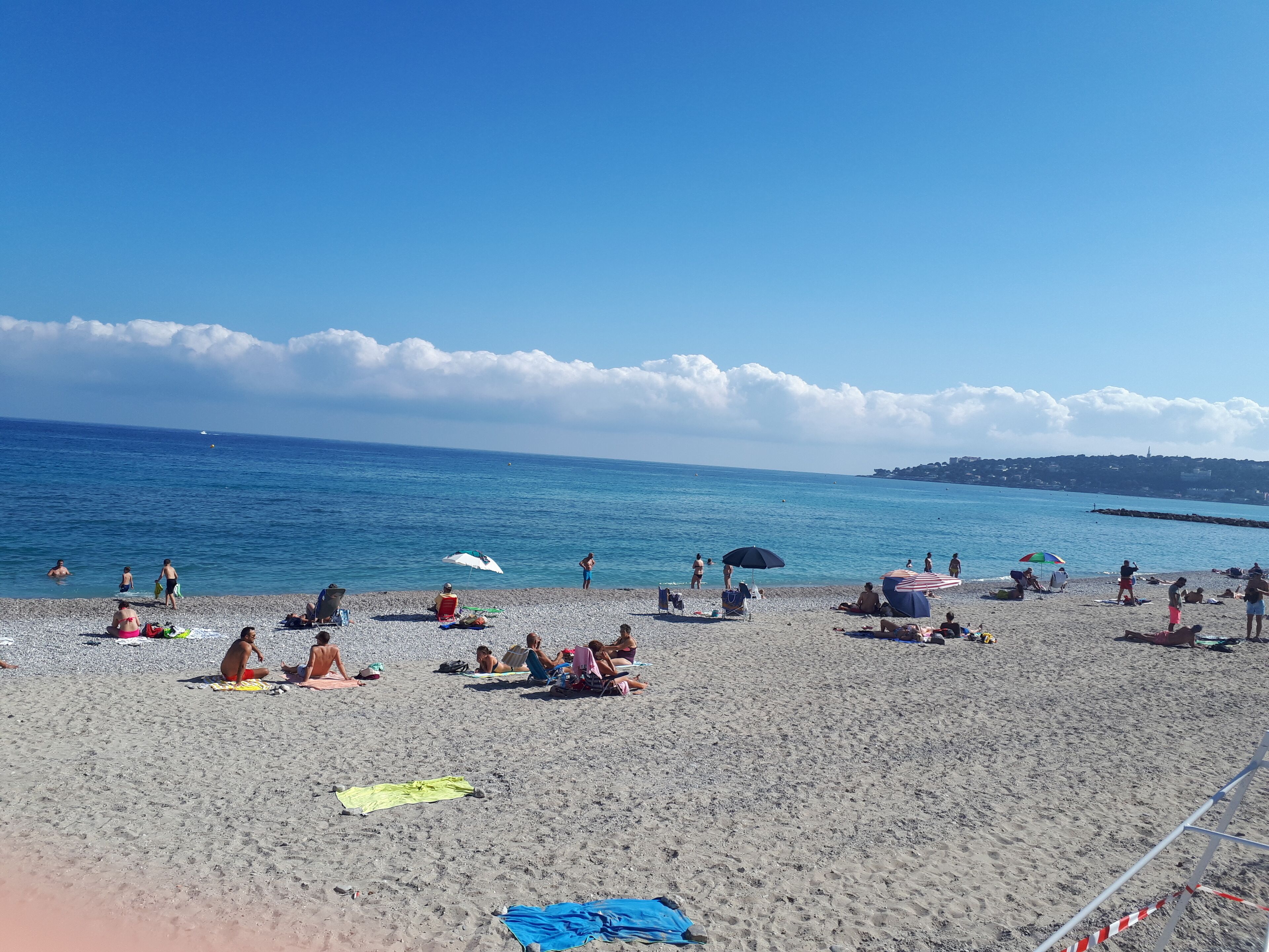 Une plage où l’on peut voir des gens bronzer et se baigner, des parasols et un ciel dégagé.