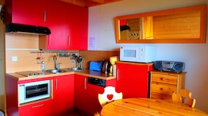 Una cocina compacta con armarios rojos, un microondas, un tostador y una mesa de madera.