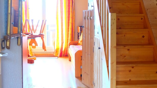 A wooden staircase leading to an upper level, a wooden bench, and a window with curtains.