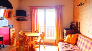 A cozy room with a wooden table, chairs, a sofa, a television, and a window with curtains.