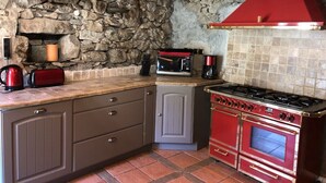 A kitchen with a stone wall, a red stove, and a microwave. - Alpine chalet, near ski resort, for 10 people, completely renovated. (Montgellafrey)
