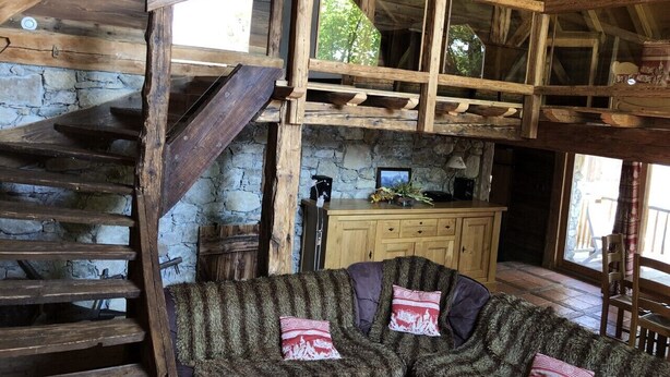 A rustic cabin interior with a stone wall, wooden staircase, and a cozy seating area with cushions. - Alpine chalet, near ski resort, for 10 people, completely renovated. (Montgellafrey)