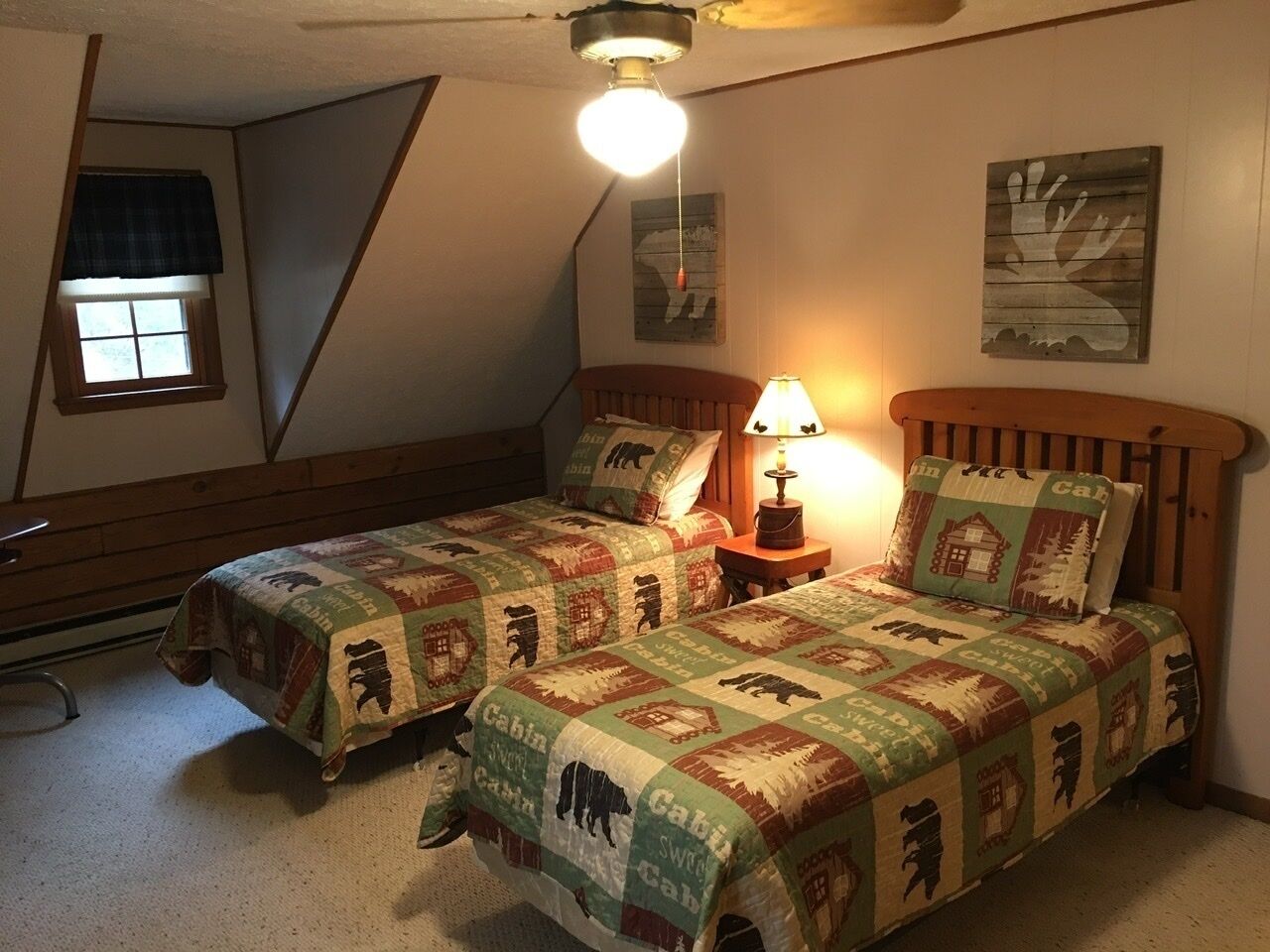 A bedroom with two beds, a ceiling fan, a lamp, and a window with blinds.