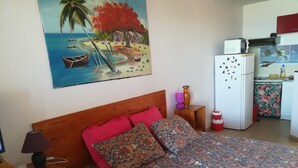 A bedroom with a wooden bed, a nightstand, a lamp, and a painting of a beach scene. - STUDIO ANSE MITAN TROIS ILETS MARTINIQUE (Trois Ilets)
