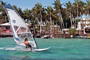 A person windsurfing on a clear day with palm trees and a building in the background. - STUDIO ANSE MITAN TROIS ILETS MARTINIQUE (Trois Ilets)