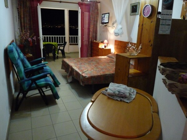 A room with a bed, a table, a chair, a TV, and a balcony with curtains. - STUDIO ANSE MITAN TROIS ILETS MARTINIQUE (Trois Ilets)